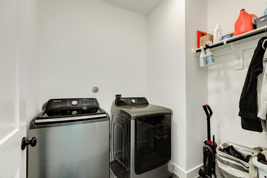 The laundry room, located at the top of the stairs, is a spacious area featuring a clothes rack and storage space.