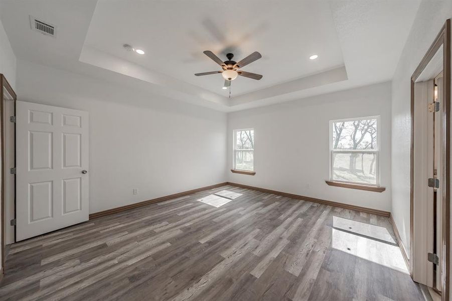 Unfurnished bedroom featuring a tray ceiling, visible vents, a ceiling fan, wood finished floors, and baseboards