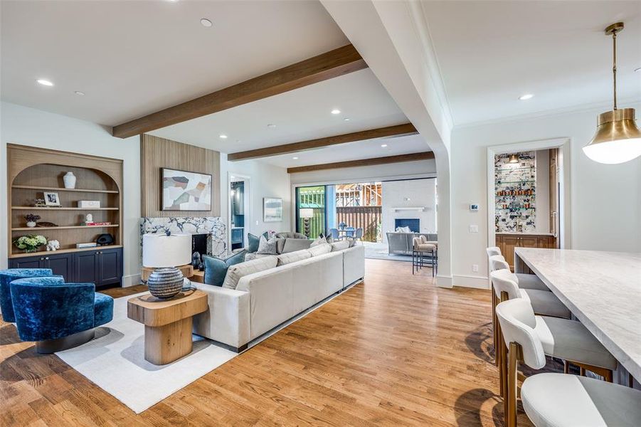 Living room featuring a large fireplace, light wood-style flooring, beam ceiling, built in shelves, and recessed lighting Living room featuring a large fireplace, light wood-style flooring, beam ceiling, built in shelves, and recessed lighting