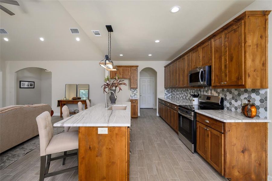 Kitchen with hanging light fixtures, a center island with sink, appliances with stainless steel finishes, light hardwood / wood-style flooring, and sink