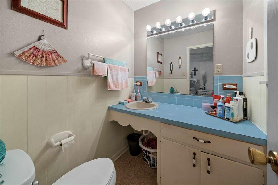 Half bath with tile patterned flooring, wainscoting, tile walls, and vanity