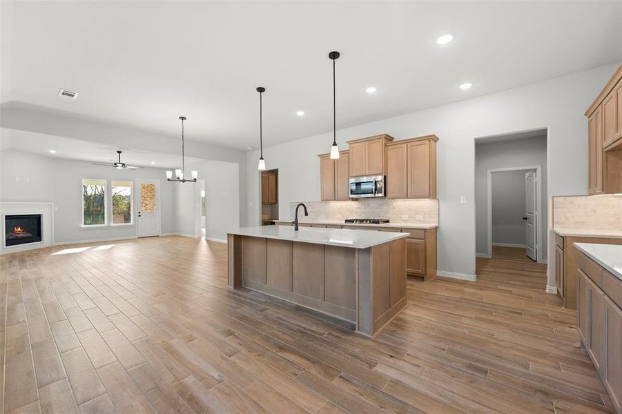 Kitchen featuring a chandelier, a warm lit fireplace, backsplash, decorative light fixtures, and recessed lighting Kitchen featuring a chandelier, a warm lit fireplace, backsplash, decorative light fixtures, and recessed lighting
