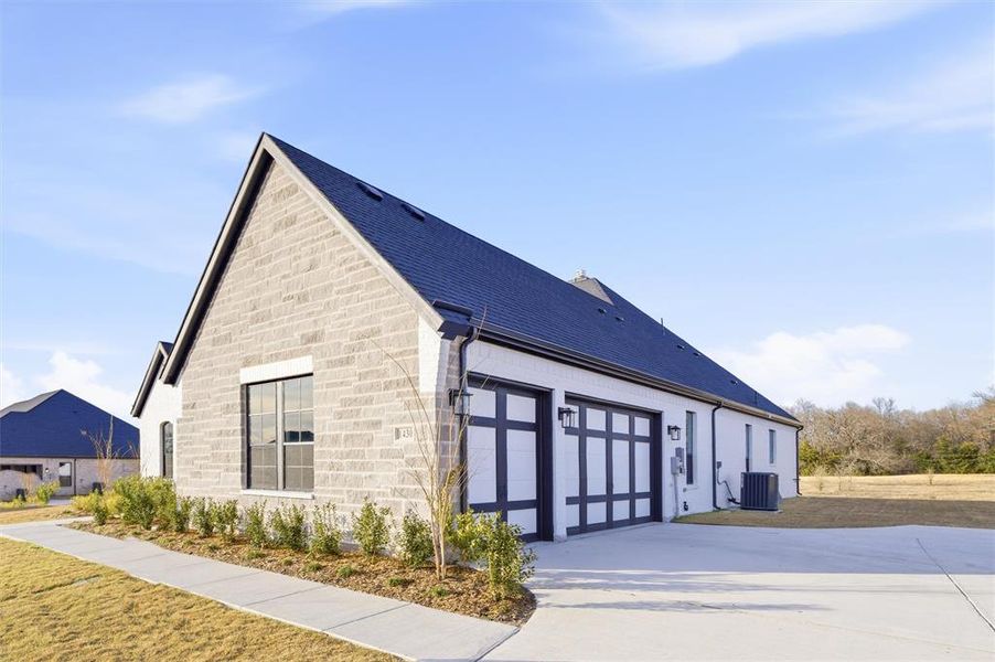 View of home's exterior with stone siding, an attached garage, roof with shingles, and concrete driveway