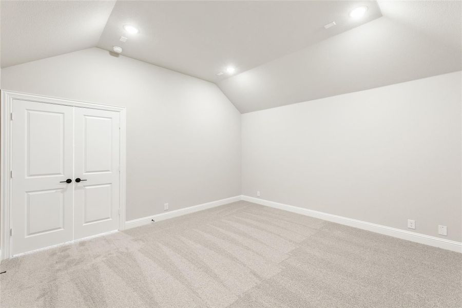 Empty bedroom with vaulted ceiling, recessed lighting, carpet flooring, and double closet doors Empty bedroom with vaulted ceiling, recessed lighting, carpet flooring, and double closet doors