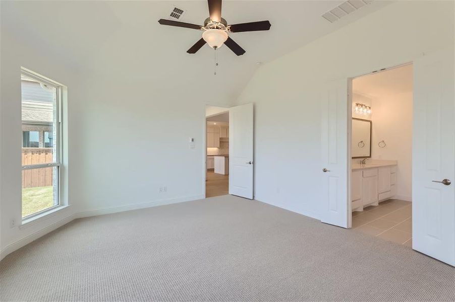 Unfurnished bedroom featuring ceiling fan, vaulted ceiling, ensuite bathroom, light colored carpet, and sink