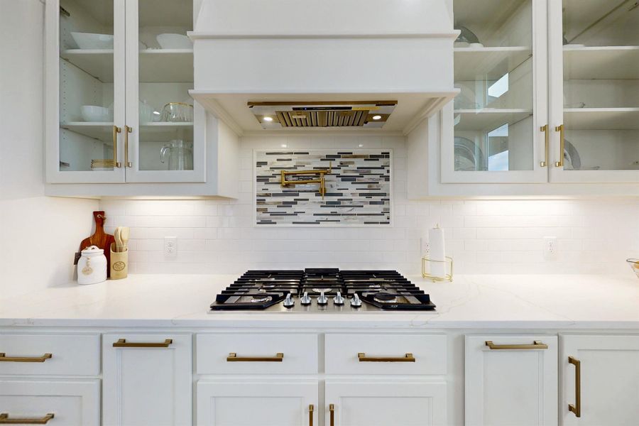 The stove top is located in the kitchen with a designer backsplash.  The Pot filler blends right in. with a powerful venthood above. Put all your special things behind clear glass for display. This kitchen with custom hardware has so many designer features. There's nothing 'cookie cutter' about this kitchen. Must see cabinetry....