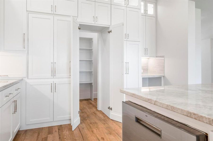 Kitchen with white cabinets, decorative backsplash, light stone counters, and light wood-type flooring