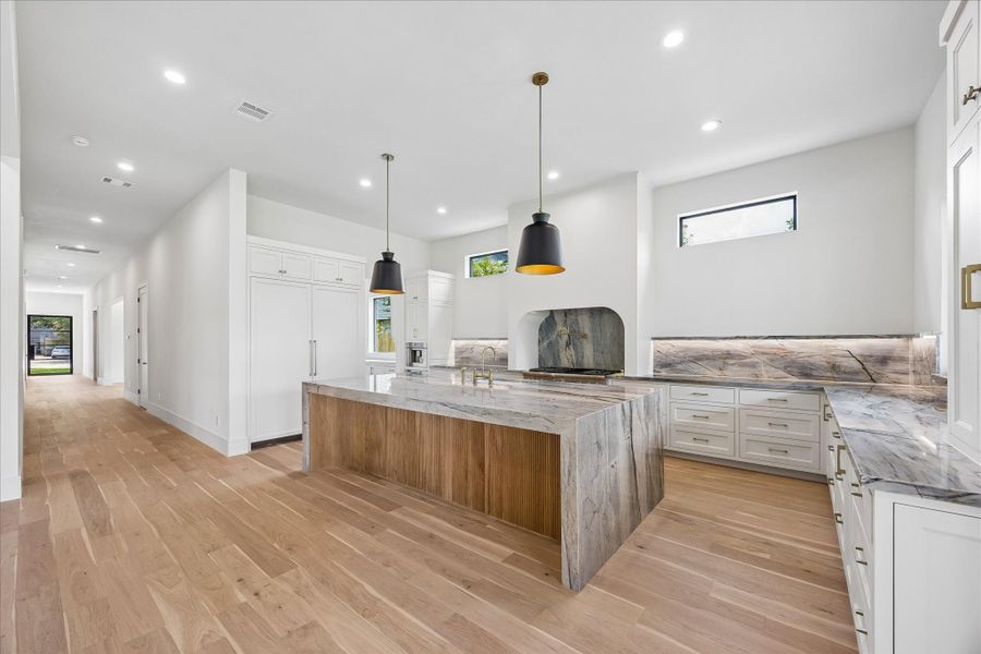 Anchored by a dramatic waterfall island with warm wood detailing, this chef’s kitchen blends timeless design with exceptional craftsmanship. Natural stone surfaces, fully inset custom cabinetry, statement lighting, and a panel ready Thermador fridge/freezer combo create a space that’s as beautiful as it is thoughtfully designed.