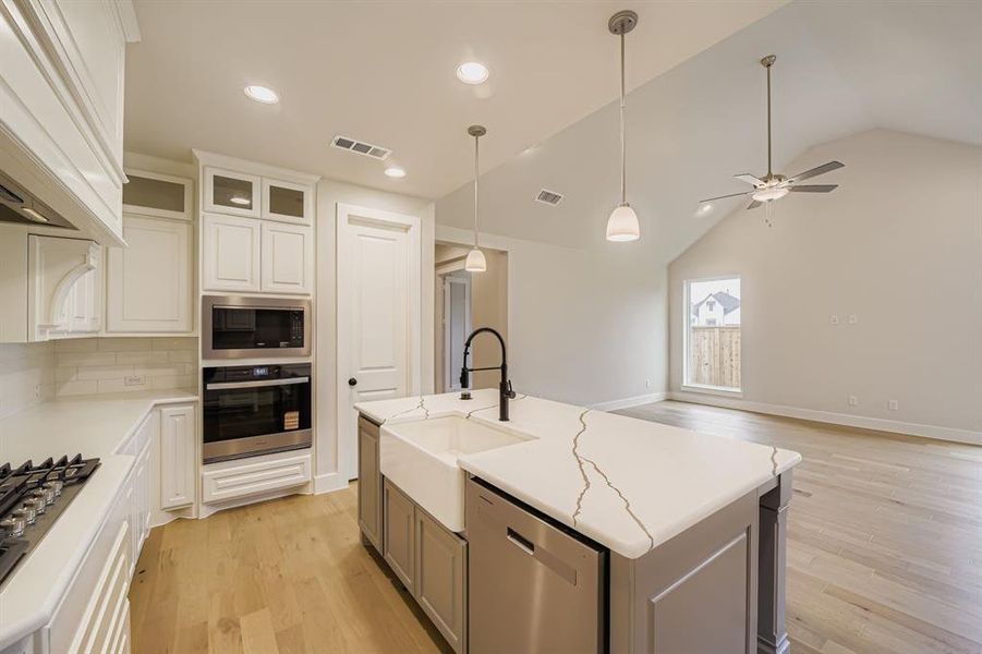 Kitchen with stainless steel appliances, tasteful backsplash, decorative light fixtures, light wood-type flooring, and vaulted ceiling