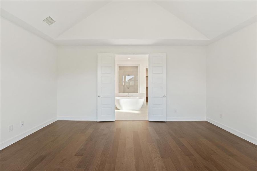 Unfurnished bedroom featuring dark wood-style floors, high vaulted ceiling, and ensuite bath
