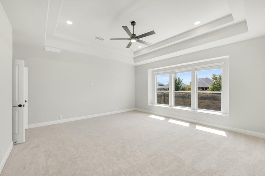 Empty bedroom with tray ceiling, ceiling fan, carpet flooring, and large triple window with natural light Empty bedroom with tray ceiling, ceiling fan, carpet flooring, and large triple window with natural light