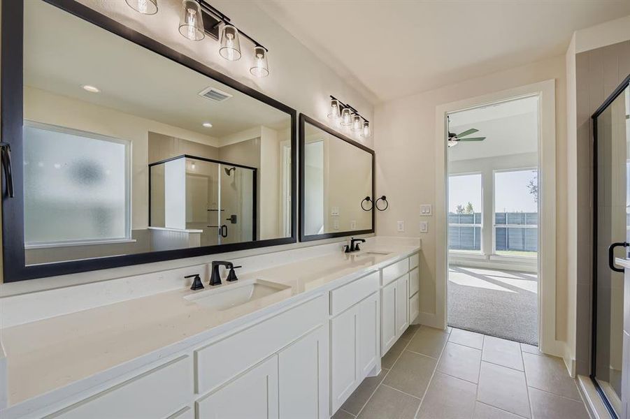 Main bath featuring light tile patterned flooring, a stall shower, double vanity, light colored carpet, and a ceiling fan