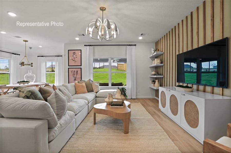 Spacious living area featuring light wood-finish flooring, a contemporary chandelier, recessed lighting, and large windows Spacious living area featuring light wood-finish flooring, a contemporary chandelier, recessed lighting, and large windows