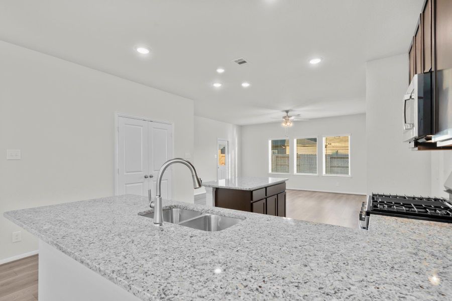 This view of the kitchen highlights the expansive island with a deep undermount stainless sink and seating space ideal for casual dining or conversation. Recessed lighting and large windows fill the home with warmth and natural light from every angle. This view of the kitchen highlights the expansive island with a deep undermount stainless sink and seating space ideal for casual dining or conversation. Recessed lighting and large windows fill the home with warmth and natural light from every angle.