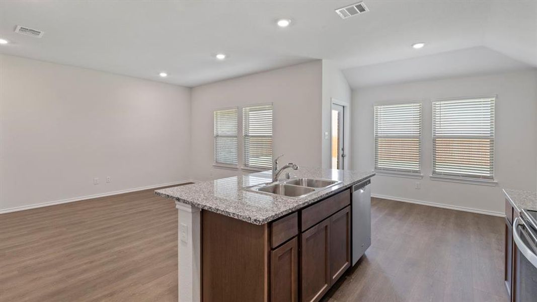 Open-concept kitchen and living area featuring wood-finish flooring, recessed lighting, and multiple windows with blinds