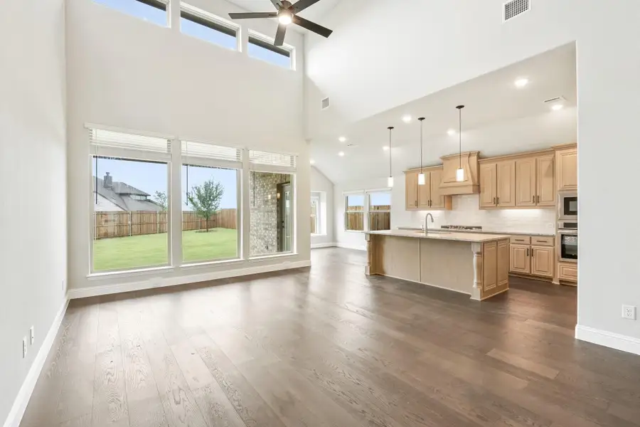 Open living area with two-story ceiling and hardwood floors flowing into kitchen with island and light wood cabinets Open living area with two-story ceiling and hardwood floors flowing into kitchen with island and light wood cabinets