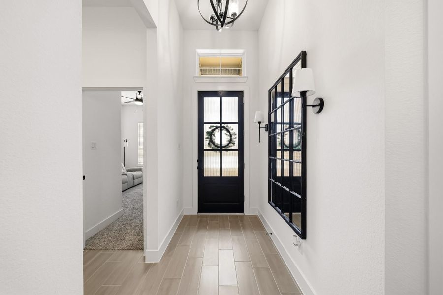 The grand entry sets a refined tone with an elegant decorative chandelier and rich wood-like tile flooring, creating a warm, sophisticated welcome as it flows seamlessly toward the guest bedrooms.