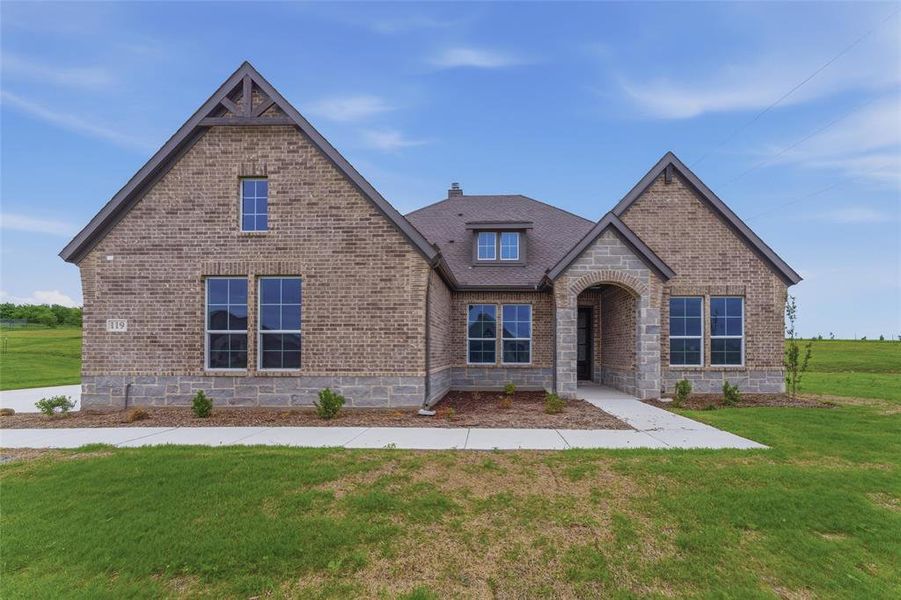 Brick and stone exterior featuring varied rooflines, an arched entryway, multiple windows, and a concrete pathway