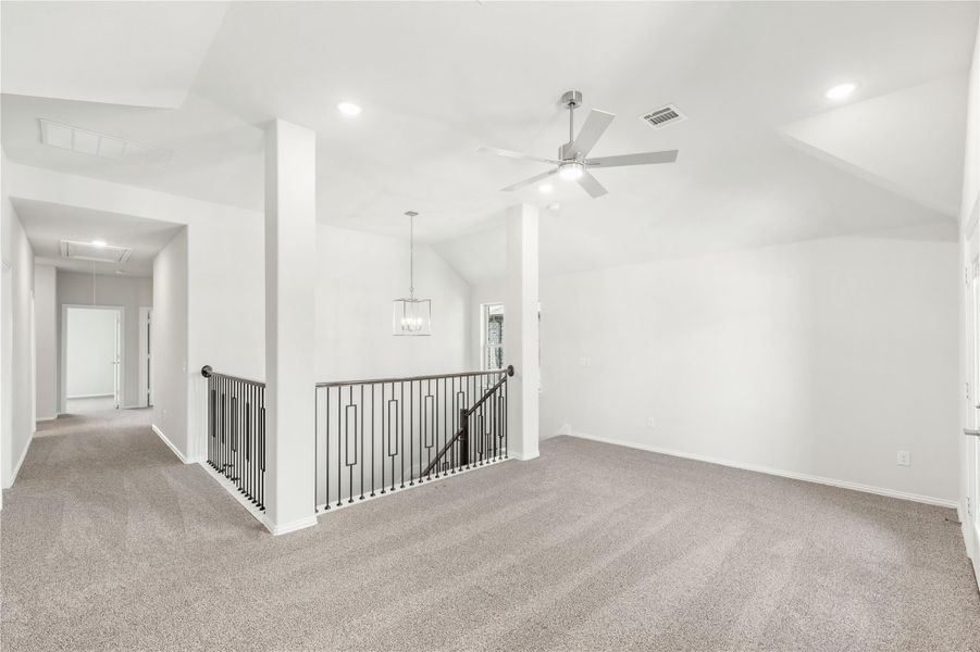 Open upstairs loft with vaulted ceiling, ceiling fan, carpet, and iron stair railing