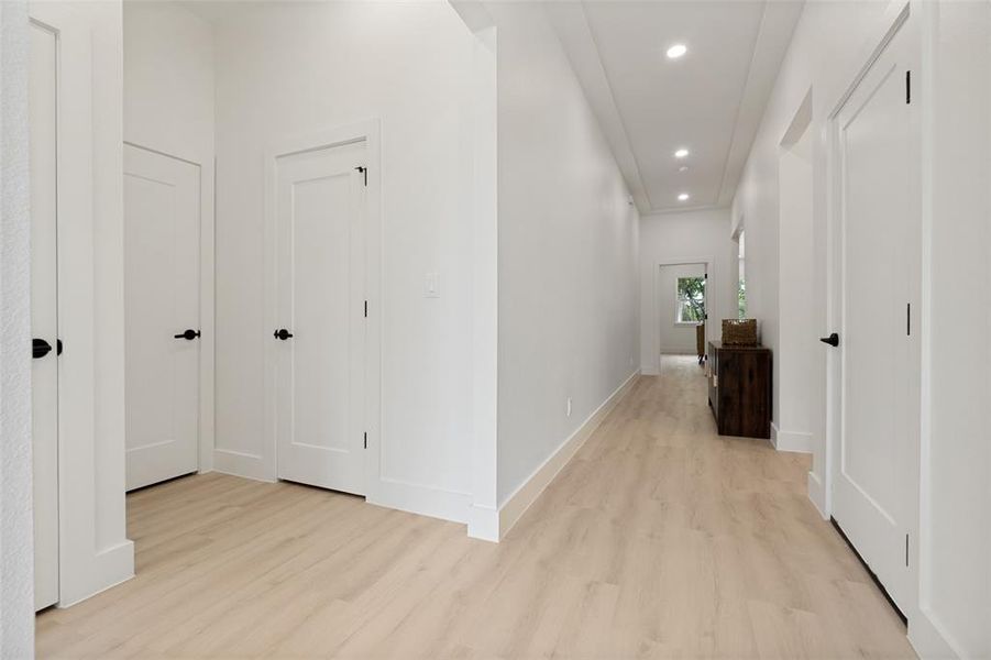 Hallway featuring light wood-finish flooring, white walls, recessed ceiling lighting, and multiple white panel doors with black hardware