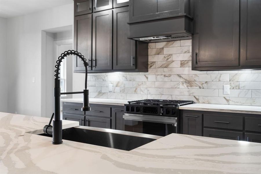 Kitchen featuring stainless steel gas stove, light stone counters, ventilation hood, backsplash, and dark brown cabinets