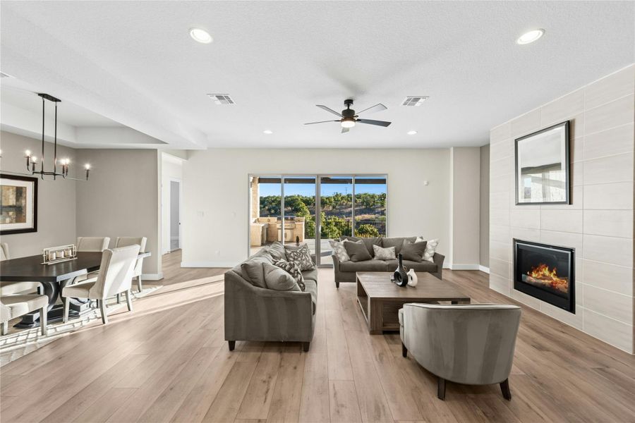 Living area featuring light wood-type flooring, recessed lighting, a tile fireplace, a chandelier, and a ceiling fan Living area featuring light wood-type flooring, recessed lighting, a tile fireplace, a chandelier, and a ceiling fan