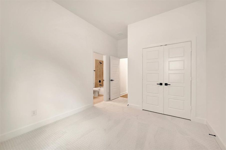 Spacious room featuring light-toned carpet flooring, white walls, and a pair of paneled closet doors with black hardware