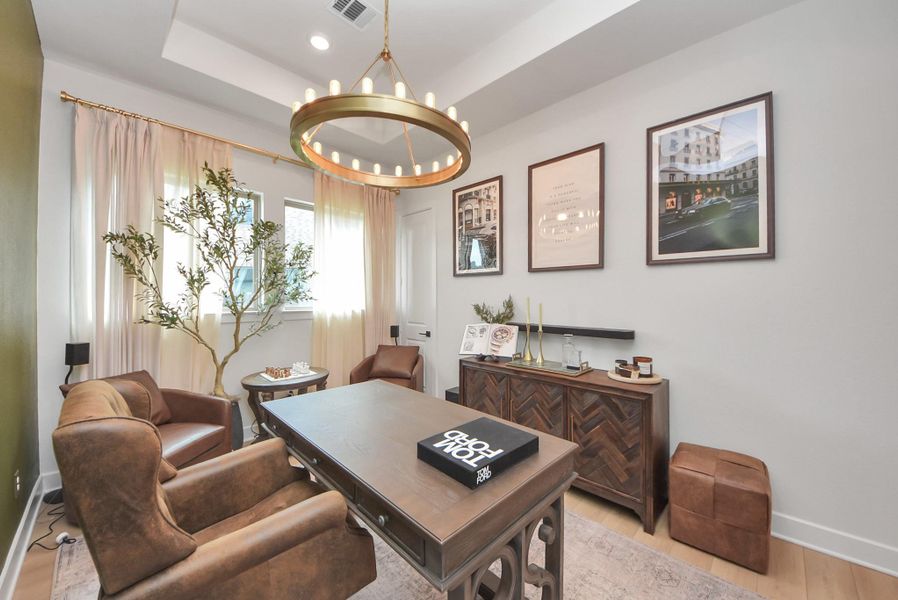 Elegant home office featuring a sophisticated chandelier, rich wood furnishings, and cozy leather chairs, complemented by tasteful artwork and natural light.