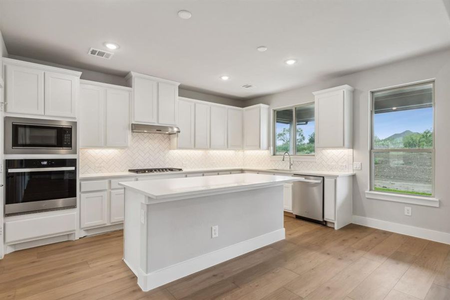 Kitchen with white cabinets, light hardwood / wood-style floors, and stainless steel appliances