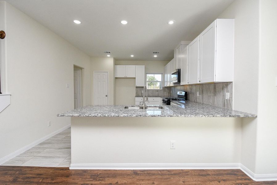 Modern kitchen with white cabinets, granite countertops, stainless steel appliances, and a mix of tile and hardwood flooring.