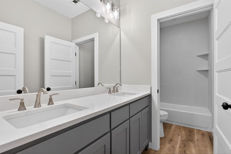 Secondary bathroom features tub/shower combo with custom tile, dual vanities, and ability to close off toilet room apart from the vanities.