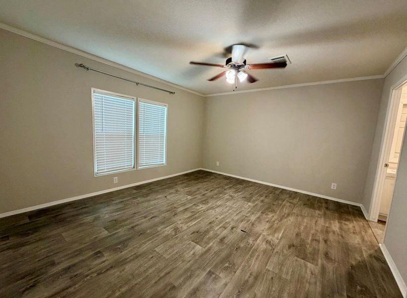 Spacious room featuring wood-finish flooring, two large windows with blinds, a ceiling fan with integrated lighting, and neutral wall paint