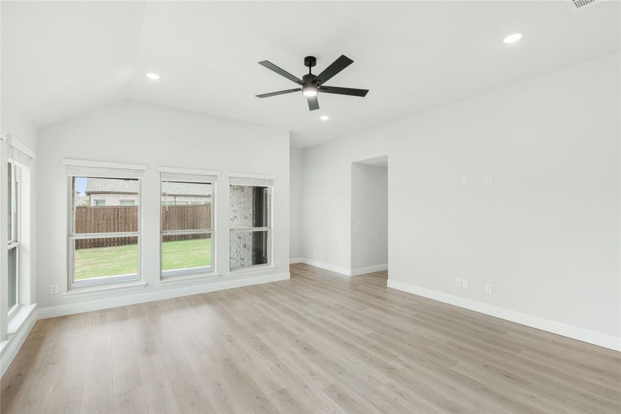Empty living room with light wood floors, ceiling fan, recessed lighting, and large windows overlooking backyard