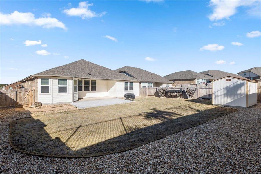 Back of house with a storage shed, a fenced backyard, an outbuilding, and a patio