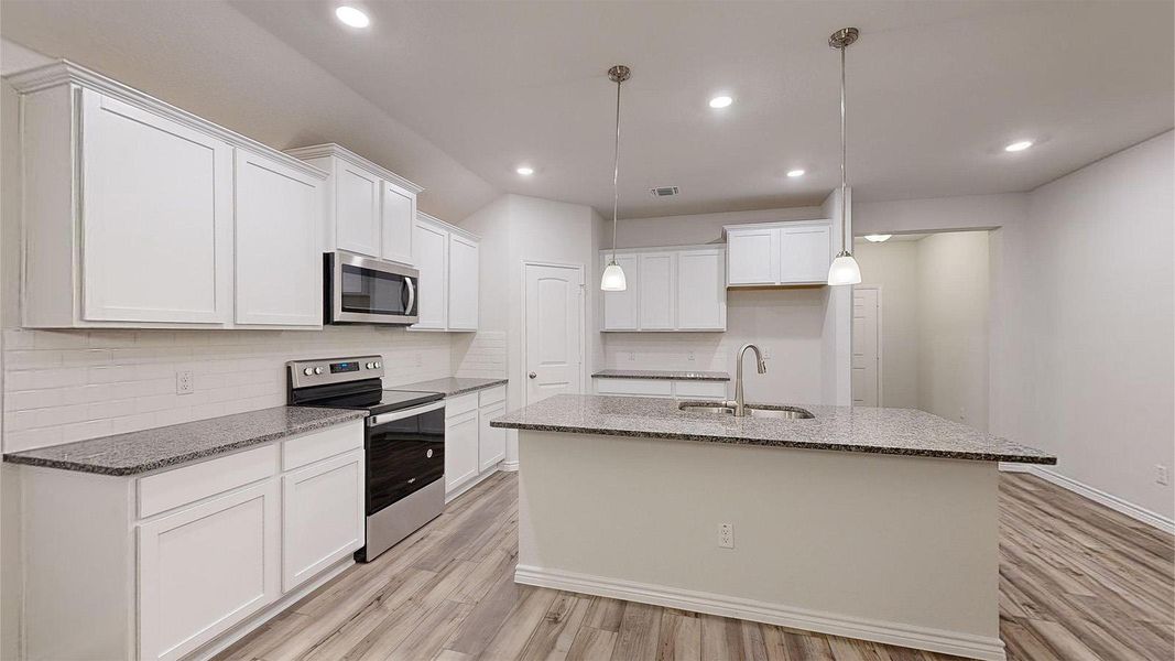 Kitchen with dark stone countertops, stainless steel appliances, an island with sink, and light wood-style floors