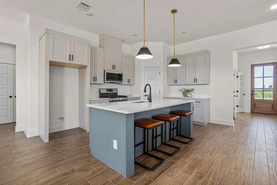 Kitchen with light hardwood / wood-style flooring, an island with sink, stainless steel appliances, backsplash, and sink