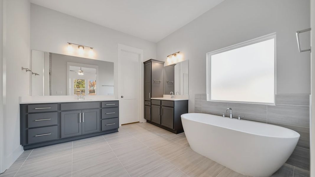 Large tiled bathroom with multiple vanities, glass shower enclosure, and freestanding tub