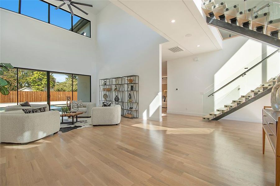 Living room with light wood finished floors, stairway, a ceiling fan, a high ceiling, and recessed lighting