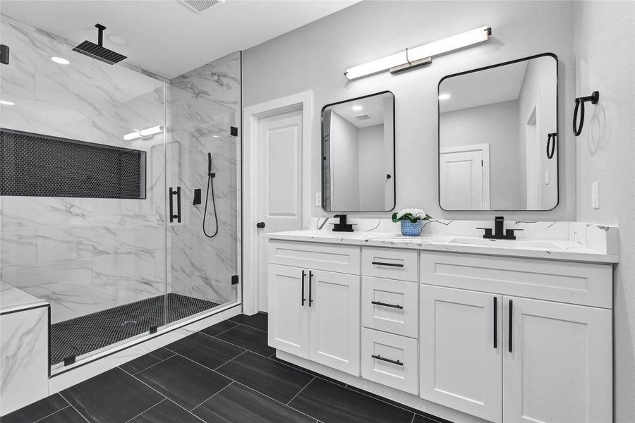 This modern bathroom features a spacious glass-enclosed shower with elegant marble-like tiles and a sleek rainfall showerhead. The double vanity includes contemporary black fixtures, large mirrors, and ample storage in white cabinets, creating a clean and stylish look.