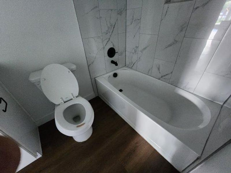 Full bath featuring dark wood finished floors and bathing tub / shower combination Full bath featuring dark wood finished floors and bathing tub / shower combination