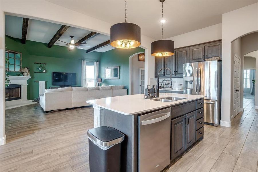 Kitchen with sink, an island with sink, decorative light fixtures, dark brown cabinets, and appliances with stainless steel finishes