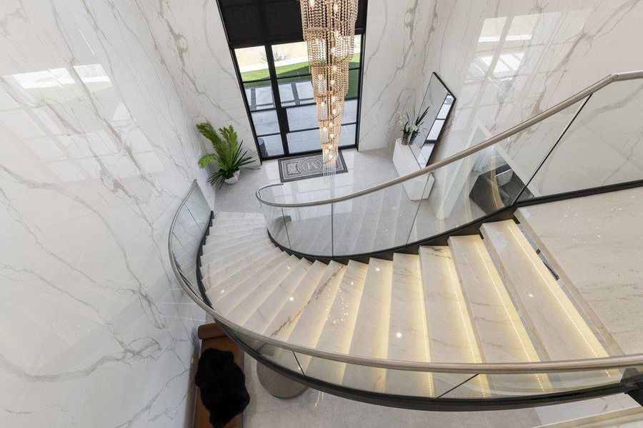 A grand, curving staircase with illuminated treads creates a dramatic entrance, complemented by sleek glass railings.
