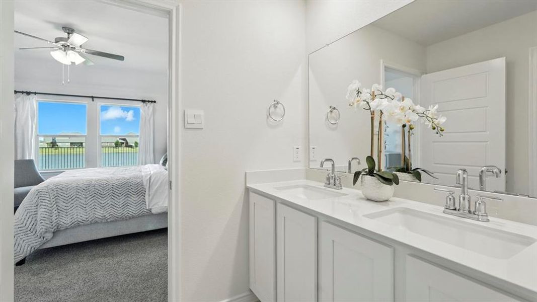 Ensuite bathroom featuring double vanity, light colored carpet, and a ceiling fan