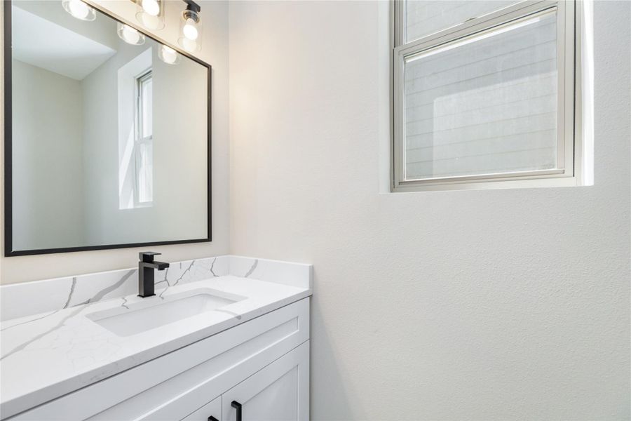 The beautiful contrast of white and black seen in the kitchen carries into the bathrooms, where a sleek white vanity with quartz countertop is complemented by bold black fixtures. A large framed mirror and ample natural light create a bright and inviting atmosphere.