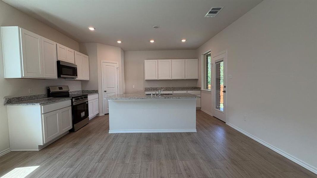 Open-concept kitchen featuring an island, recessed lighting, wood-finish flooring, white cabinetry, and stainless steel appliances Open-concept kitchen featuring an island, recessed lighting, wood-finish flooring, white cabinetry, and stainless steel appliances