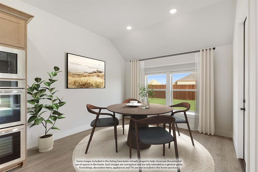 Dining area with round wood table, four chairs, vaulted ceiling, and large window overlooking backyard