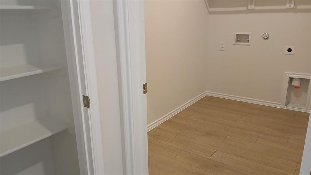 Dedicated utility space featuring wood-finish flooring, white baseboards, and neutral wall paint Dedicated utility space featuring wood-finish flooring, white baseboards, and neutral wall paint