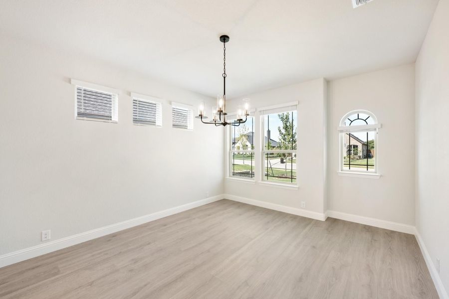 Empty dining room with light wood floors, black chandelier, and multiple windows