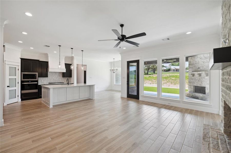 Kitchen featuring ceiling fan with notable chandelier, stainless steel appliances, light hardwood / wood-style floors, an island with sink, and decorative backsplash