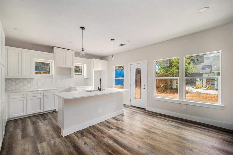 Kitchen with backsplash, dark wood-style floors, white cabinetry, a center island with sink, and hanging light fixtures